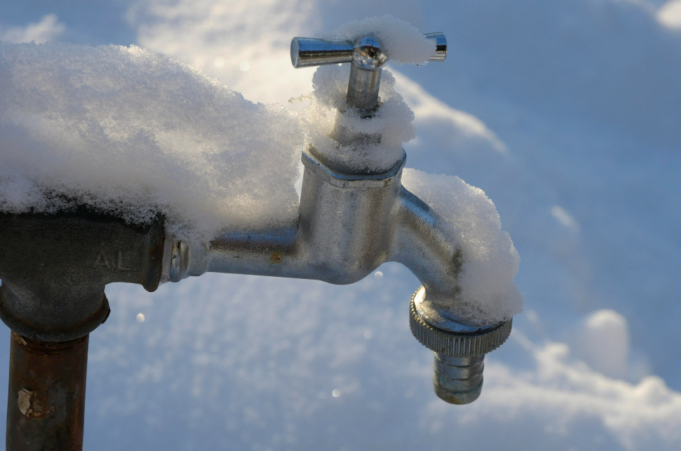 An outdoor faucet covered in snow during the winter.