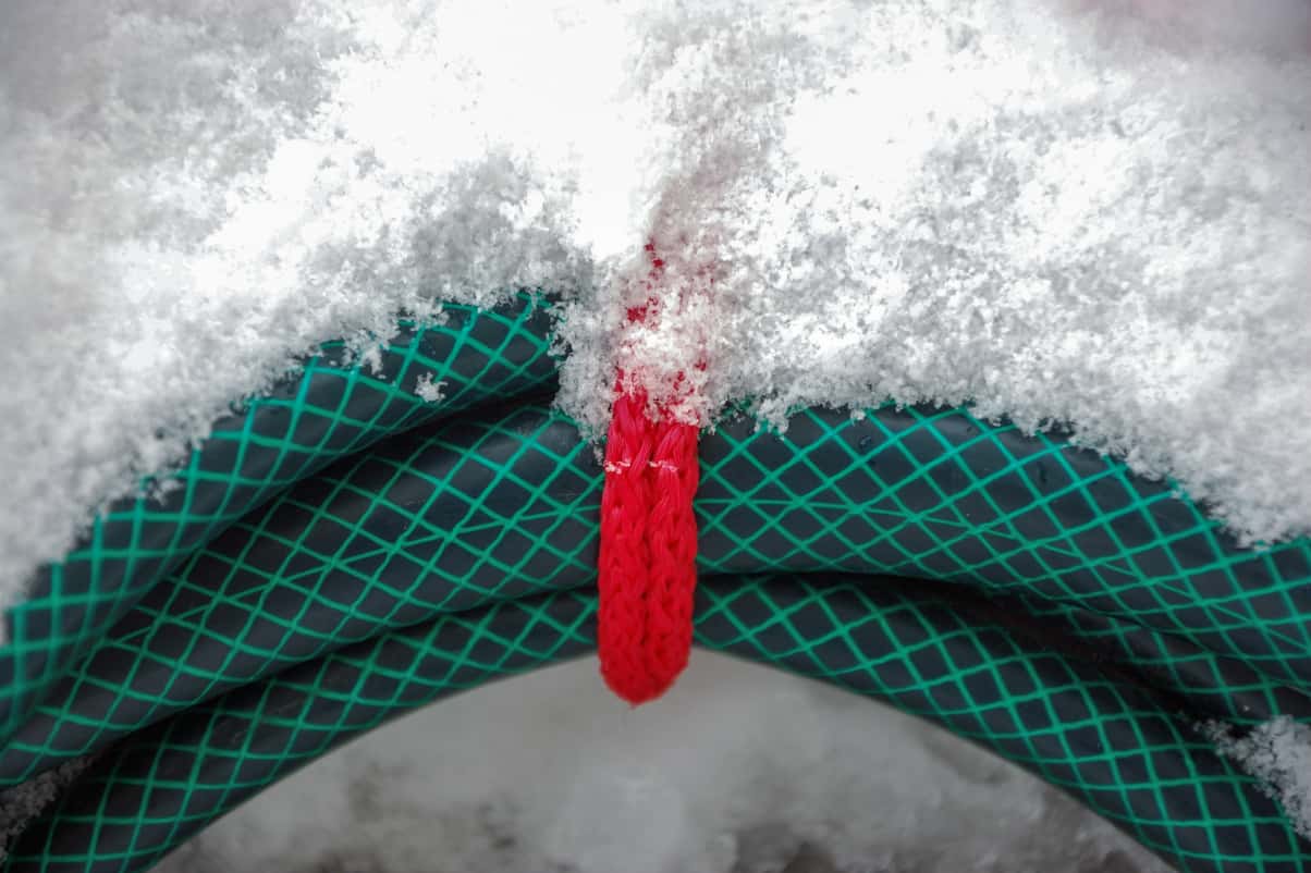 A frozen garden hose covered in snow during the winter.